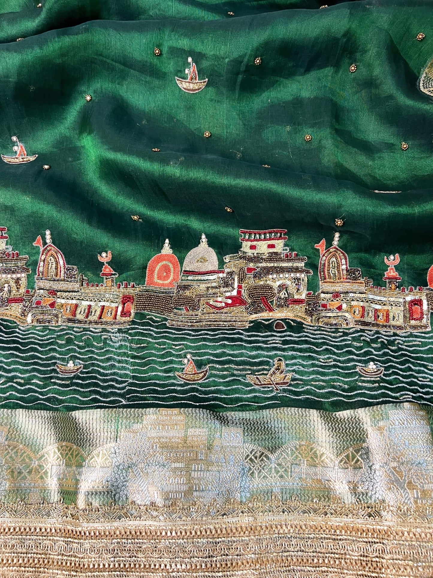 Emerald green Banarasi saree with hand embroidery of Varanasi ghats, boats, temples, and river scenes.