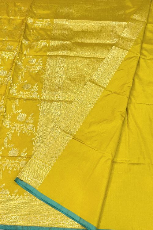 Handwoven Mustard Yellow Katan Silk Saree with intricate floral design, contrast green selvedge border, and detailed aachal. Paired with an unstitched lilac blouse with matching sleeve borders.