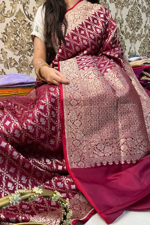 Handwoven wine color Katan silk saree with red contrast selvedge, intricate floral jaal pattern, and sona rupa zari floral border, paired with plain wine blouse piece featuring matching floral sleeve border, made in Banaras.