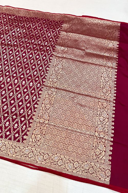 Handwoven wine color Katan silk saree with red contrast selvedge, intricate floral jaal pattern, and sona rupa zari floral border, paired with plain wine blouse piece featuring matching floral sleeve border, made in Banaras.
