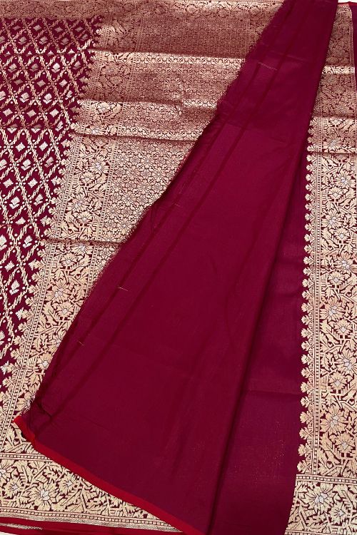 Handwoven wine color Katan silk saree with red contrast selvedge, intricate floral jaal pattern, and sona rupa zari floral border, paired with plain wine blouse piece featuring matching floral sleeve border, made in Banaras.
