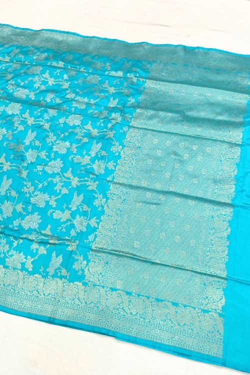 Handwoven Sky Blue Katan Silk Saree with allover floral jaal pattern, intricate sona rupa zari floral border and anchal, paired with a plain sky blue blouse piece featuring matching floral border sleeves, made in Banaras.