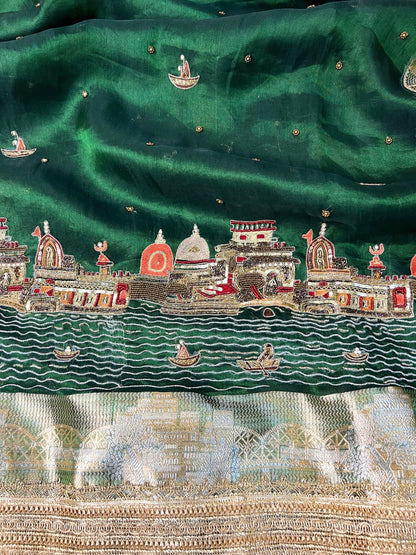 Emerald green Banarasi saree with hand embroidery of Varanasi ghats, boats, temples, and river scenes.
