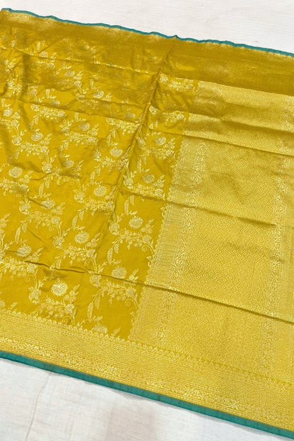 Handwoven Mustard Yellow Katan Silk Saree with intricate floral design, contrast green selvedge border, and detailed aachal. Paired with an unstitched lilac blouse with matching sleeve borders.