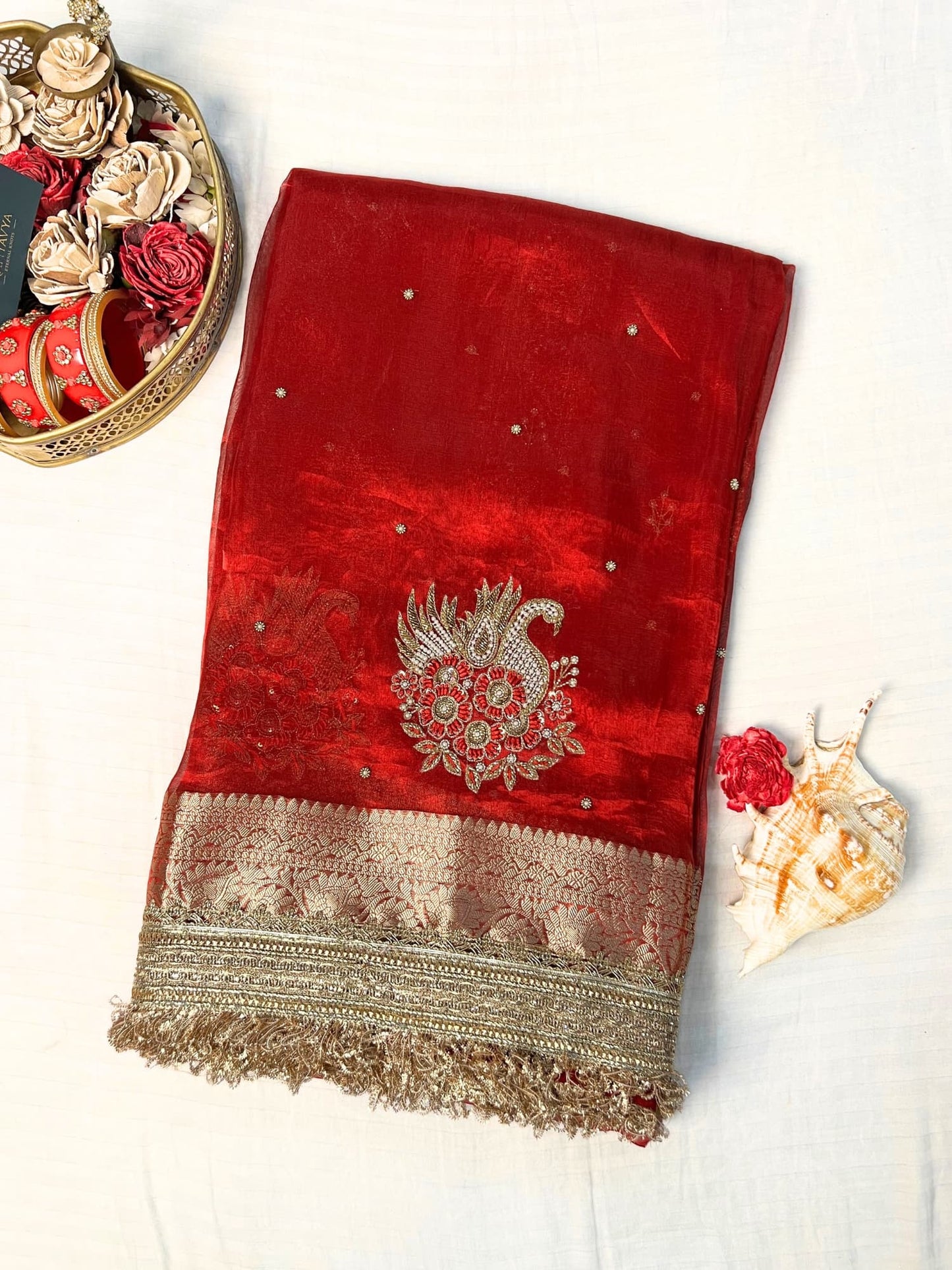"Red 100% pure Banarasi tissue silk saree featuring a beautifully embroidered white swan motif with floral detailing in silver and red. Adorned with scattered buti work, a richly woven zari pallu, and a gota patti lace border. Ideal for weddings, receptions, and festive occasions. Comes with an unstitched brocade blouse."