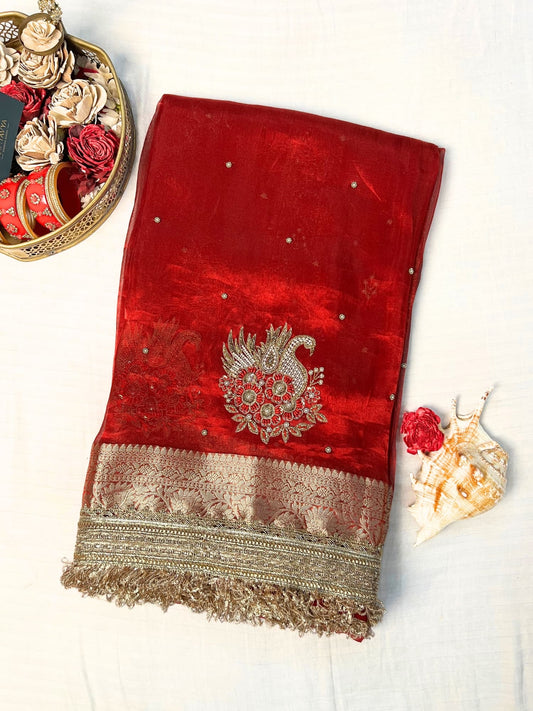 "Red 100% pure Banarasi tissue silk saree featuring a beautifully embroidered white swan motif with floral detailing in silver and red. Adorned with scattered buti work, a richly woven zari pallu, and a gota patti lace border. Ideal for weddings, receptions, and festive occasions. Comes with an unstitched brocade blouse."