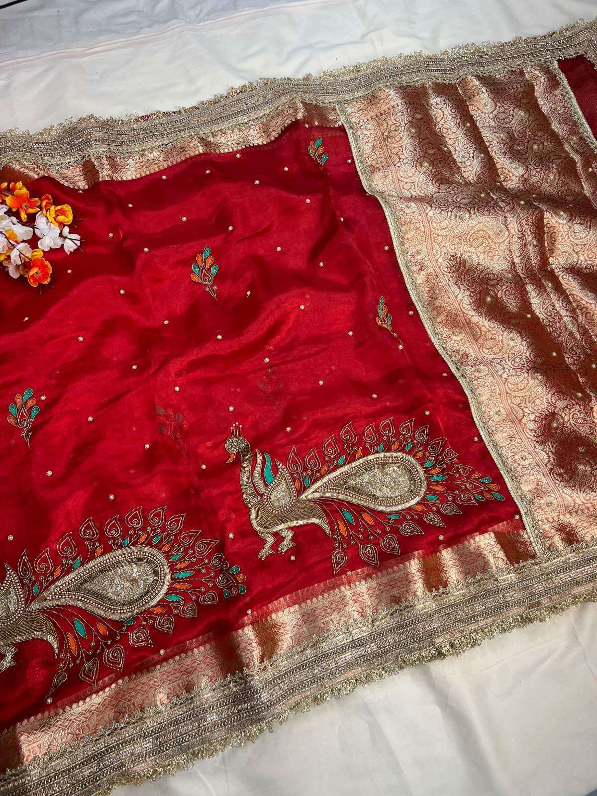 Red fabric with intricate gold embroidery featuring peacock designs on a white background.