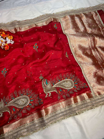Red fabric with intricate gold embroidery featuring peacock designs on a white background.