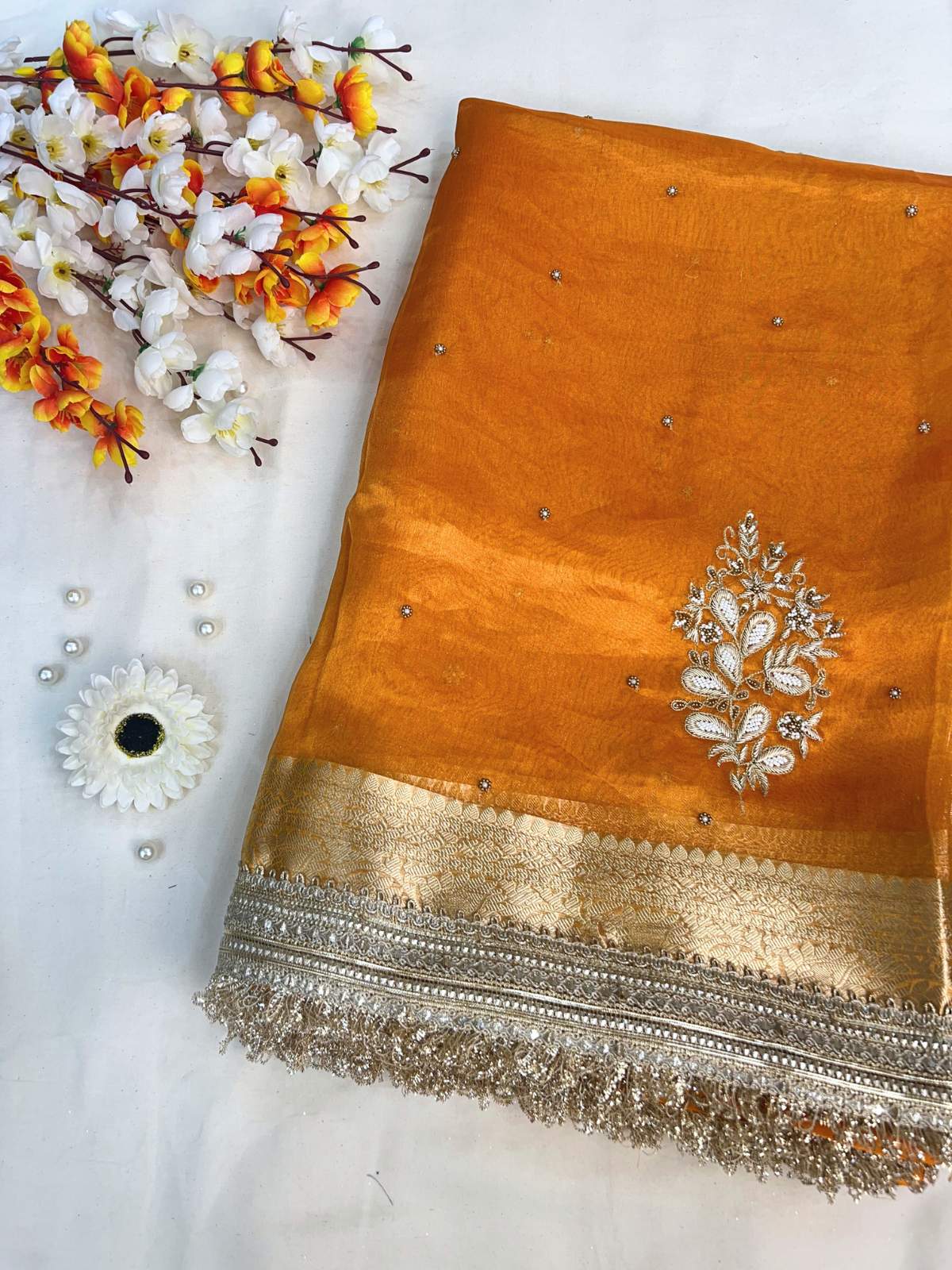 Orange saree with intricate silver embroidery on a white background with decorative flowers.
