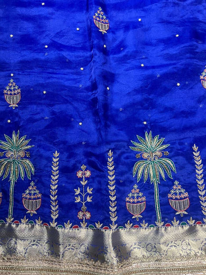 This royal blue hand-embroidered pure tissue silk saree reflects timeless Banarasi artistry and festive grandeur. Crafted in shimmering pure Banarasi tissue silk, the saree features delicate hand-embroidered kalash motifs, palm trees, floral vines, and ti