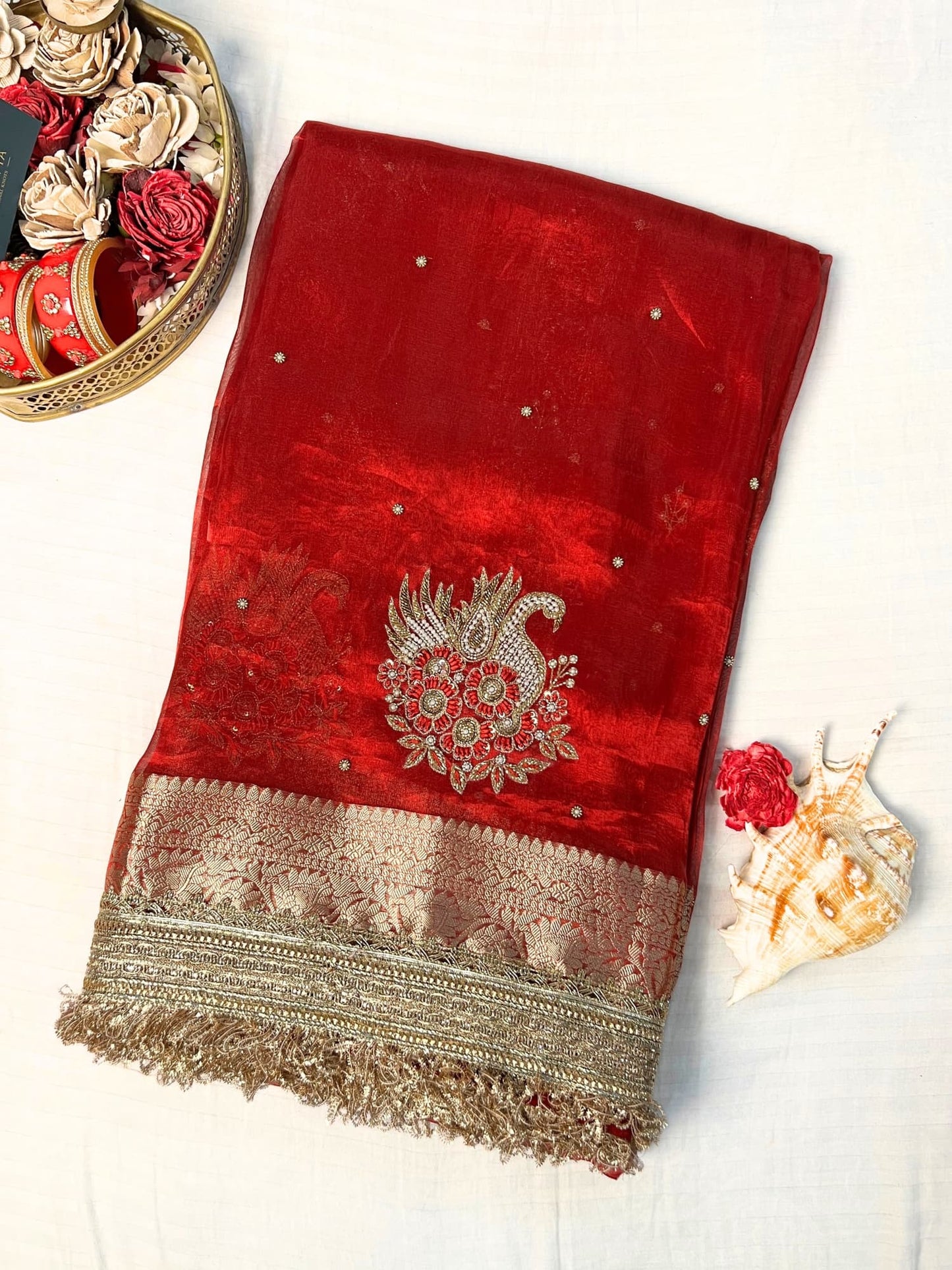 "Red 100% pure Banarasi tissue silk saree featuring a beautifully embroidered white swan motif with floral detailing in silver and red. Adorned with scattered buti work, a richly woven zari pallu, and a gota patti lace border. Ideal for weddings, receptions, and festive occasions. Comes with an unstitched brocade blouse."