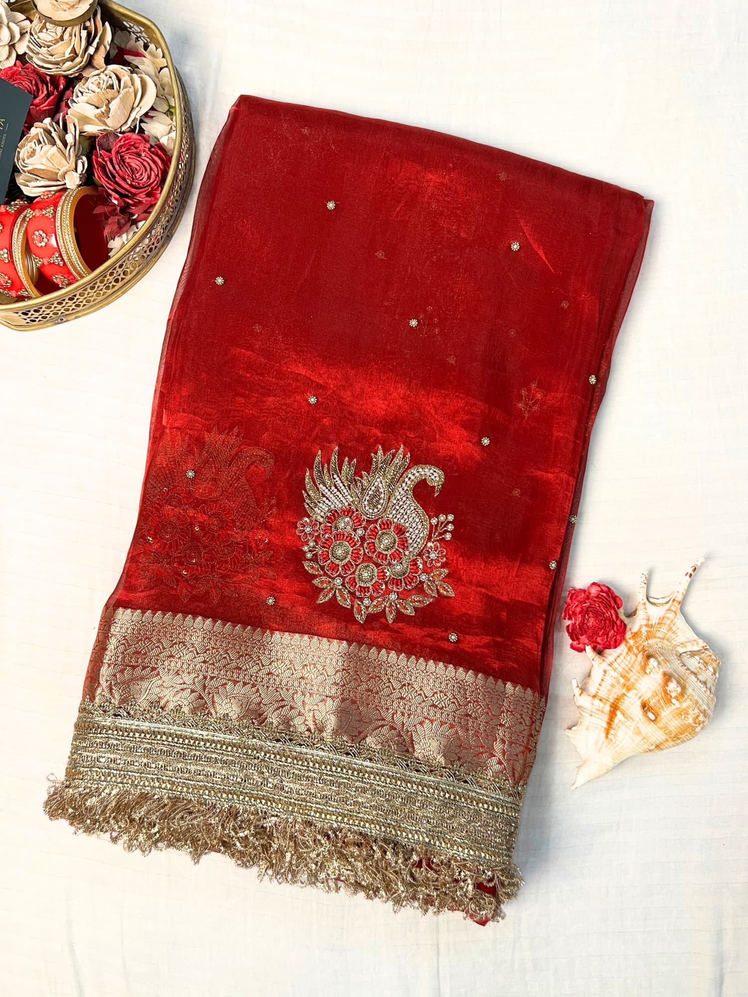 "Red 100% pure Banarasi tissue silk saree featuring a beautifully embroidered white swan motif with floral detailing in silver and red. Adorned with scattered buti work, a richly woven zari pallu, and a gota patti lace border. Ideal for weddings, receptions, and festive occasions. Comes with an unstitched brocade blouse."