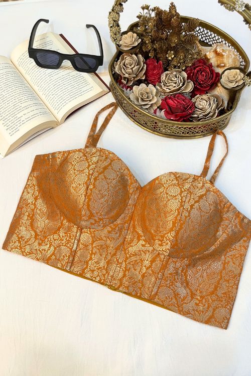 Orange Banarasi Brocade Corset with gold zari, featuring intricate floral motifs and meenakari work in a hole pattern, structured with boning, padded cups, and back lacing.