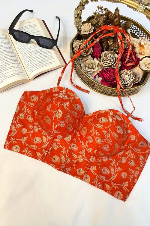 Orange Banarasi Brocade Corset with gold zari, featuring intricate floral motifs and meenakari work in a hole pattern, structured with boning, padded cups, and back lacing.