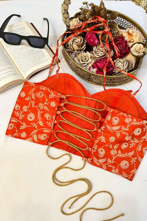 Orange Banarasi Brocade Corset with gold zari, featuring intricate floral motifs and meenakari work in a hole pattern, structured with boning, padded cups, and back lacing.