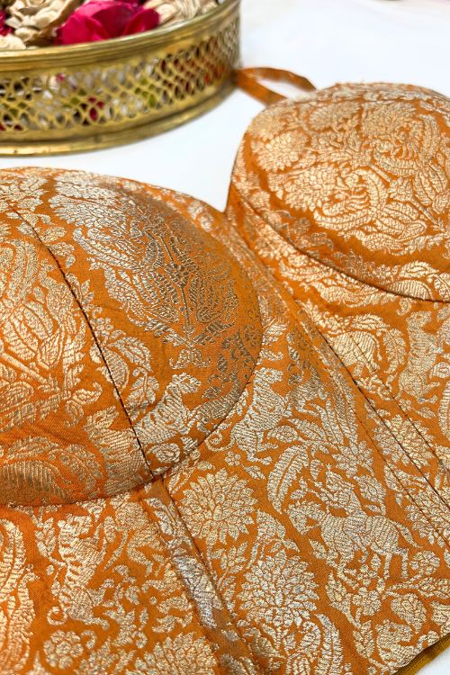 Orange Banarasi Brocade Corset with gold zari, featuring intricate floral motifs and meenakari work in a hole pattern, structured with boning, padded cups, and back lacing.