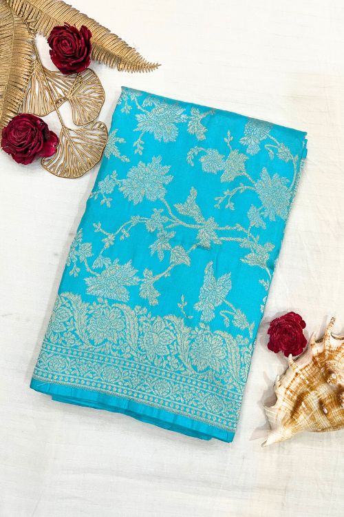 Handwoven Sky Blue Katan Silk Saree with allover floral jaal pattern, intricate sona rupa zari floral border and anchal, paired with a plain sky blue blouse piece featuring matching floral border sleeves, made in Banaras.