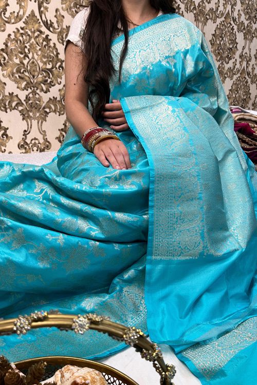 Handwoven Sky Blue Katan Silk Saree with allover floral jaal pattern, intricate sona rupa zari floral border and anchal, paired with a plain sky blue blouse piece featuring matching floral border sleeves, made in Banaras.