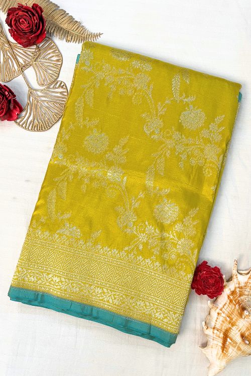 Handwoven Mustard Yellow Katan Silk Saree with intricate floral design, contrast green selvedge border, and detailed aachal. Paired with an unstitched lilac blouse with matching sleeve borders.