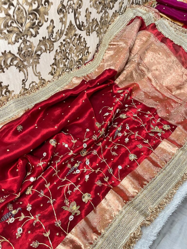 "Hand-embroidered red Banarasi tissue silk saree with intricate floral and bird motifs in gold zari and sequin work, finished with a delicate gold zari woven border."