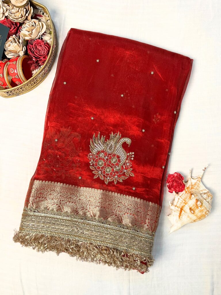 "Red 100% pure Banarasi tissue silk saree featuring a beautifully embroidered white swan motif with floral detailing in silver and red. Adorned with scattered buti work, a richly woven zari pallu, and a gota patti lace border. Ideal for weddings, receptions, and festive occasions. Comes with an unstitched brocade blouse."