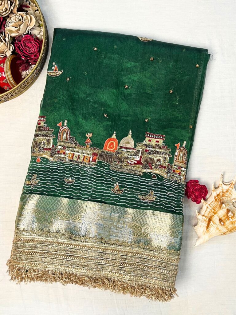 Emerald green Banarasi saree with hand embroidery of Varanasi ghats, boats, temples, and river scenes.